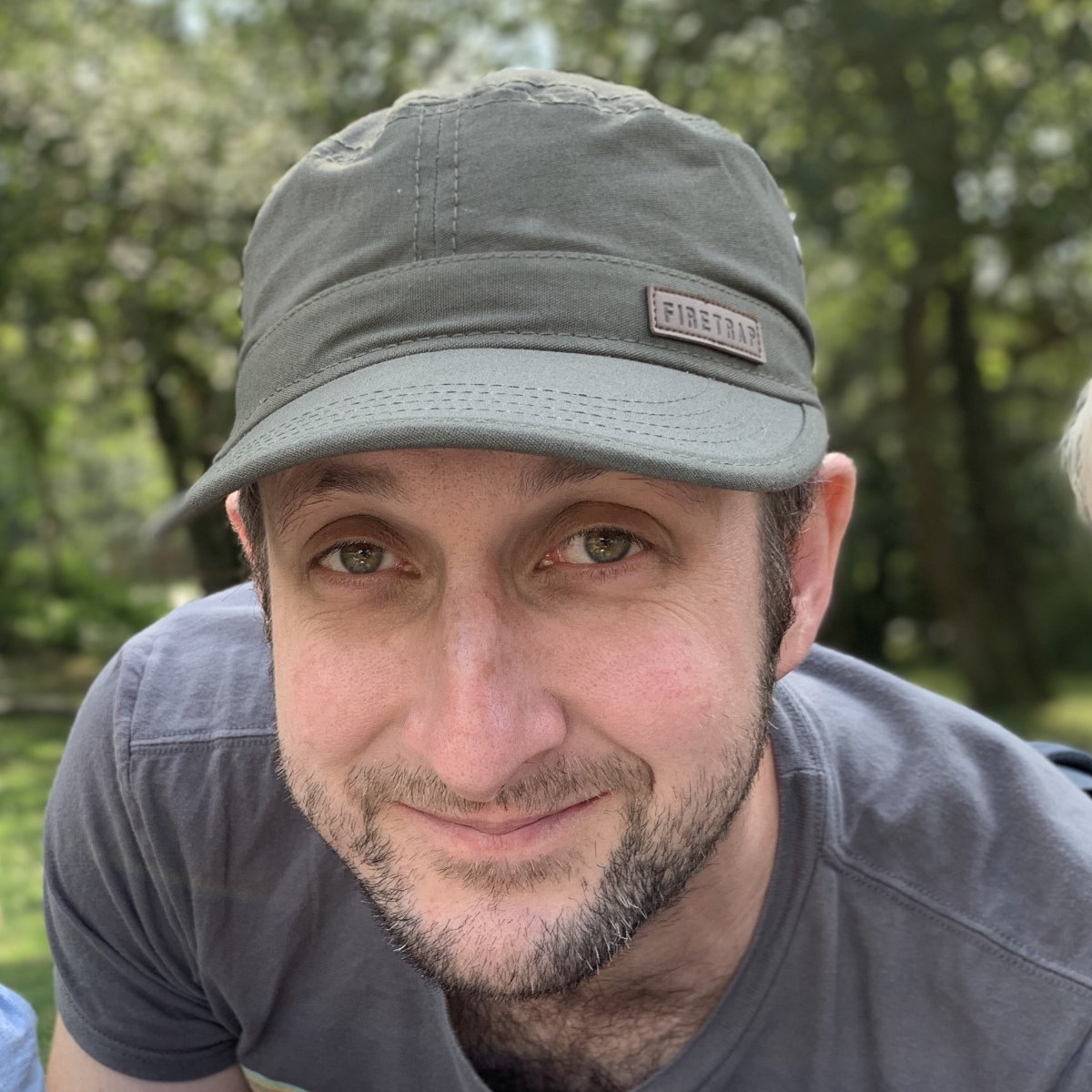 A photo of Ross wearing a khaki green cap and smiling.